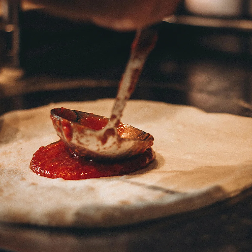 Il pomodoro steso con il mestolo sulla base della pizza